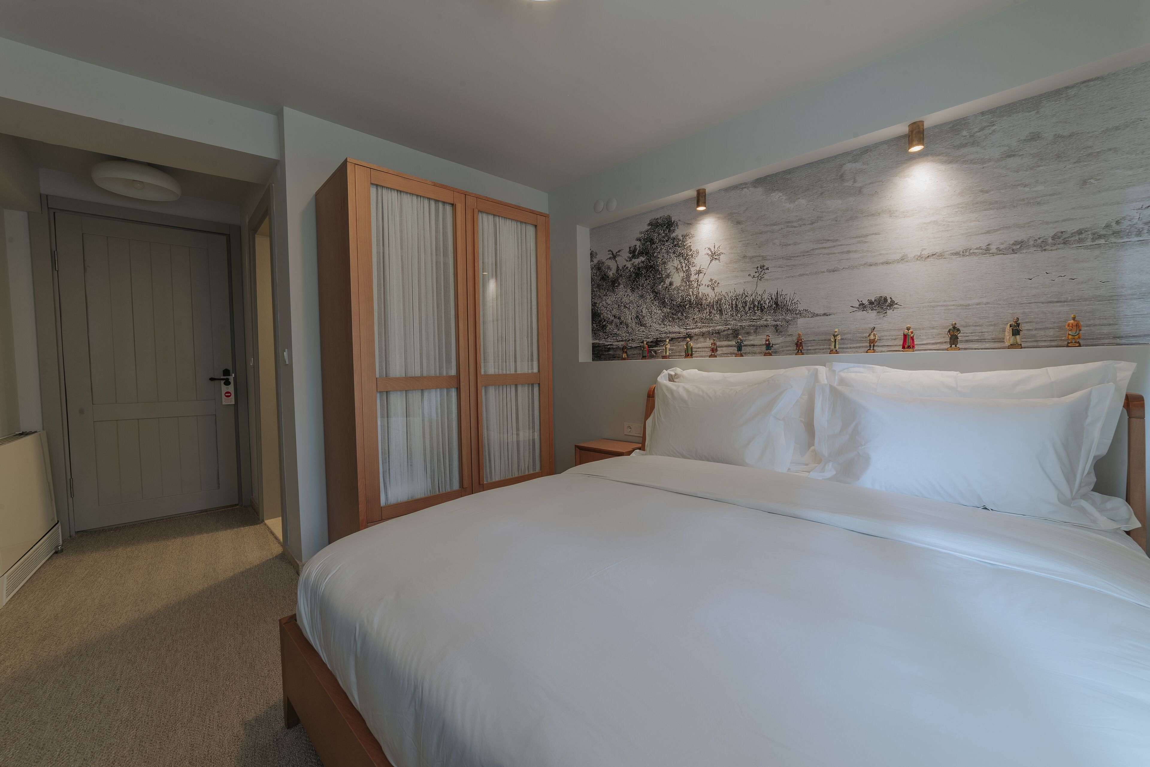A bedroom with a large bed, a wardrobe with curtains, a nightstand, and a wall with a painting.