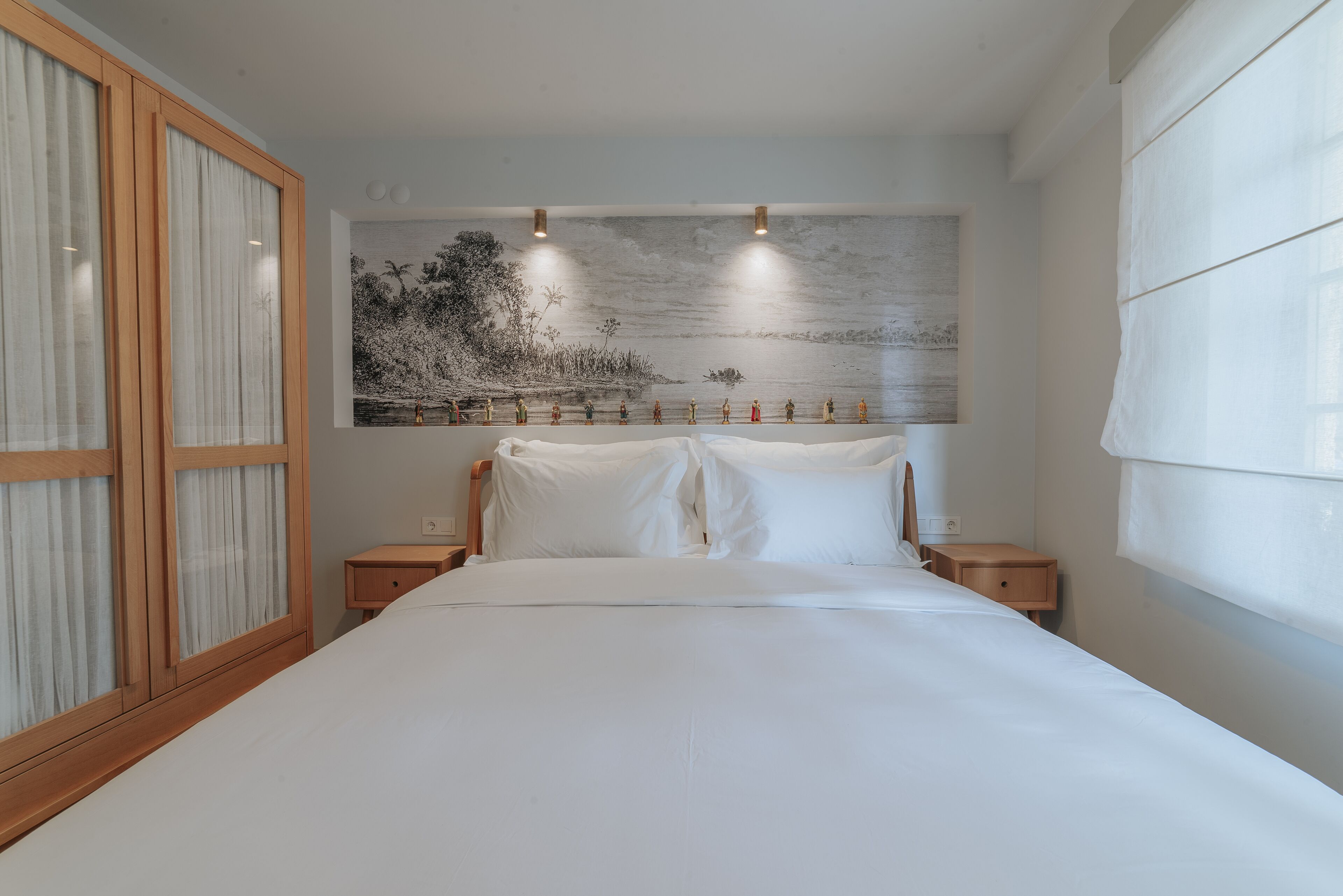 A neatly made bed with white linens, a wooden headboard, and a wall-mounted artwork depicting a landscape scene.