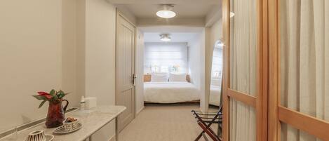 A narrow hallway leading to a bedroom with a bed, a desk with a chair, and a small table with a vase and plates.