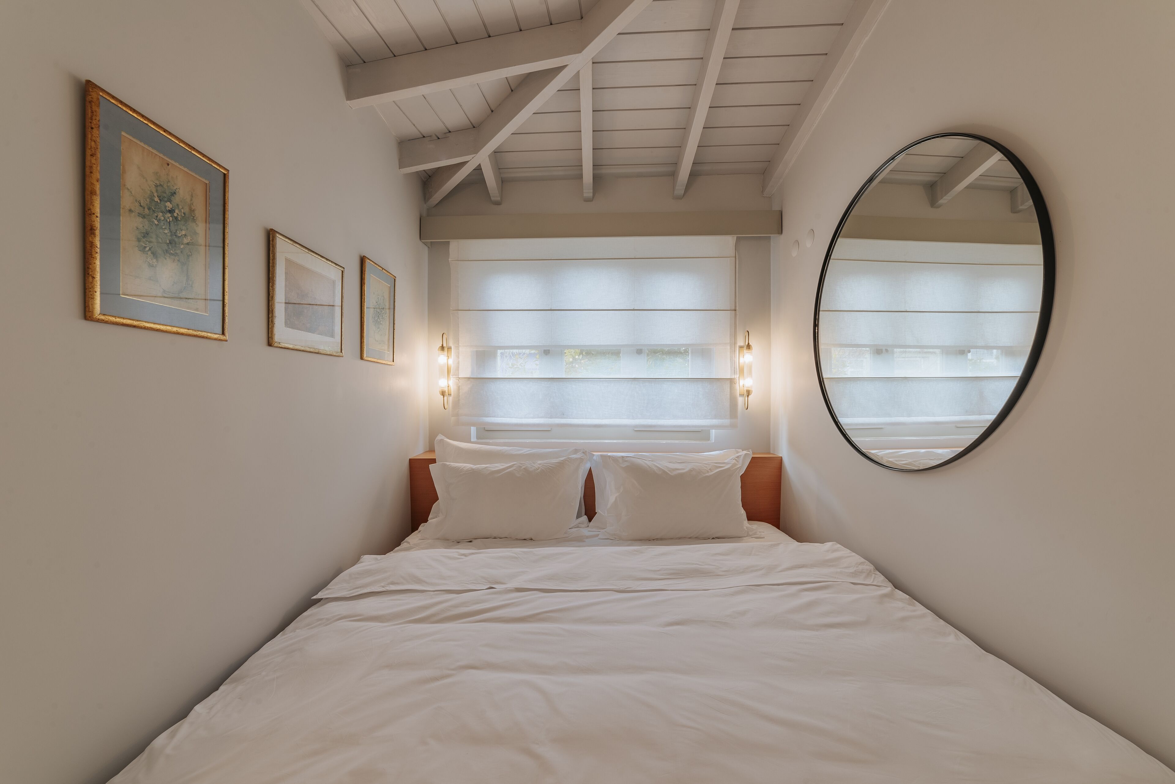 Un dormitorio con una cama, un espejo grande y tres cuadros en la pared.