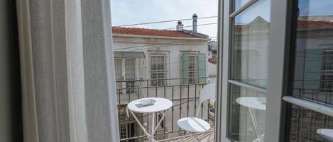 Varanda com mesa e cadeira brancas, telhado de telhas vermelhas e vista para edifícios próximos.