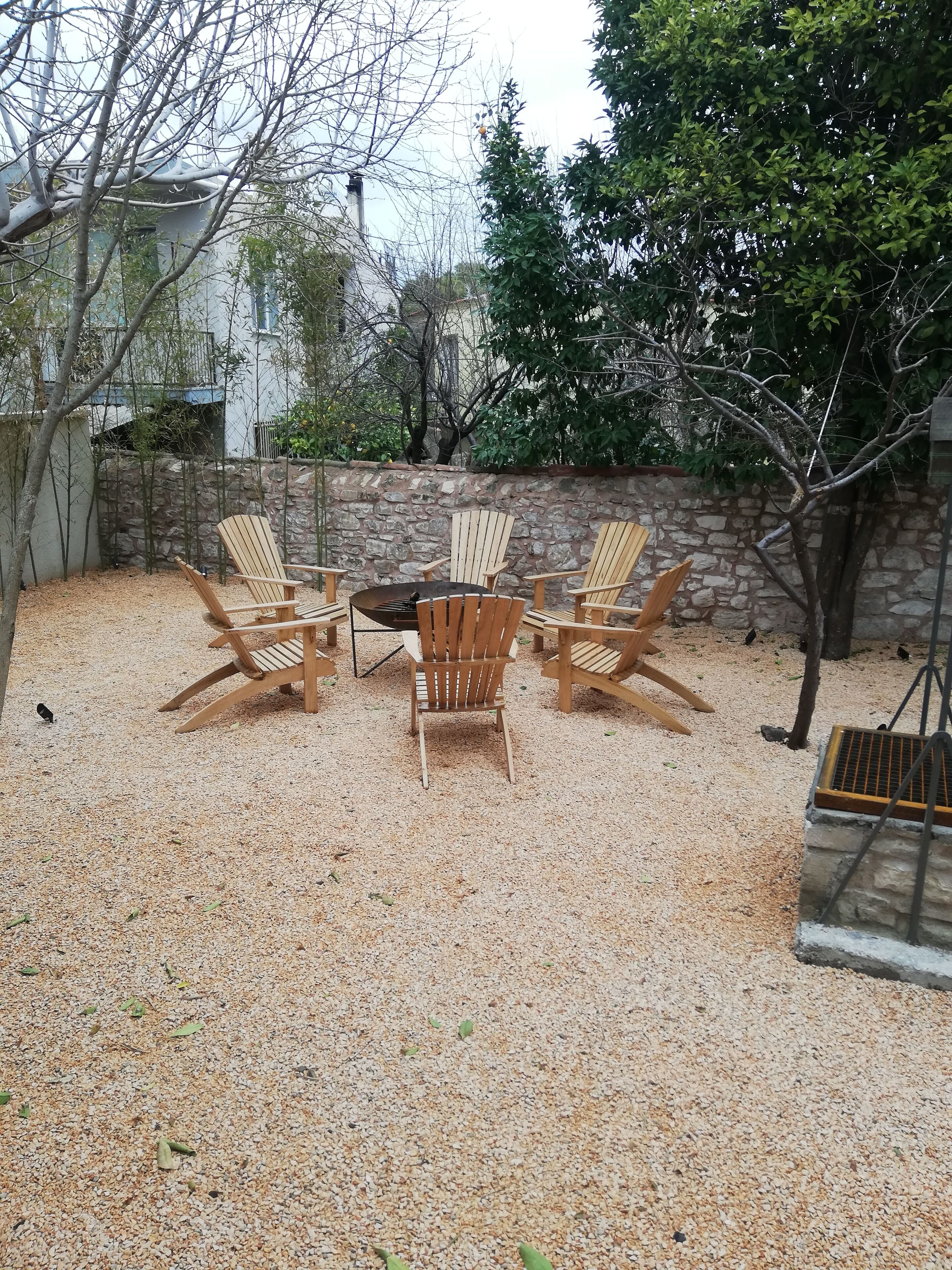 Un jardin avec un muret en pierre, un foyer et quatre fauteuils Adirondack en bois disposés autour.