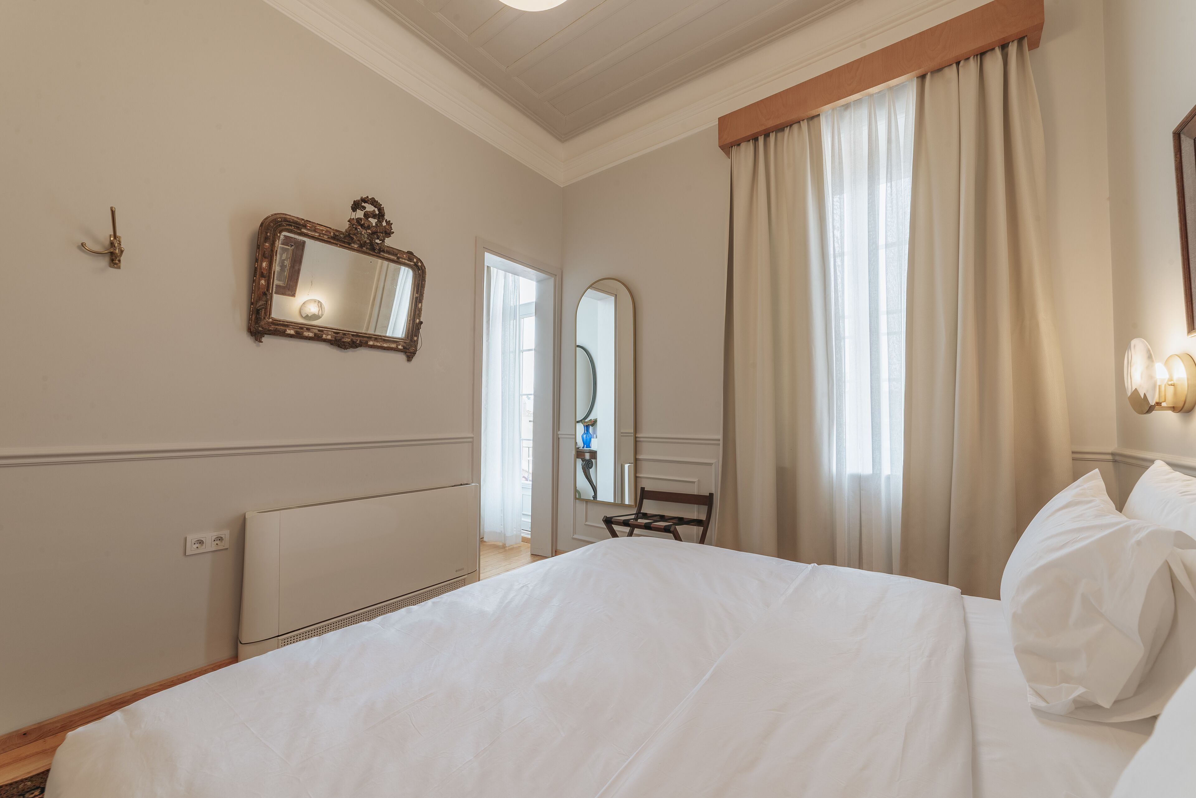 A hotel room with a large bed, a mirror, a radiator, and a window with curtains.