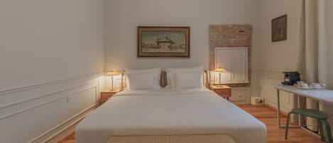 A hotel room with a large bed, two bedside tables with lamps, a desk with a coffee maker, and a painting on the wall.