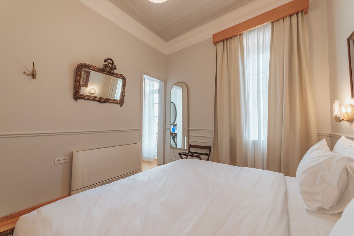 A hotel room with a large bed, a mirror, a chair, and a window with curtains.