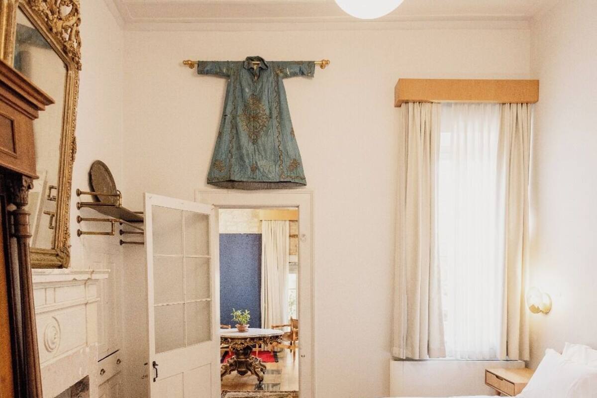 Makuuhuoneessa on puinen sänky, lipasto, peili ja vaatehenkariin ripustettu vaate.
