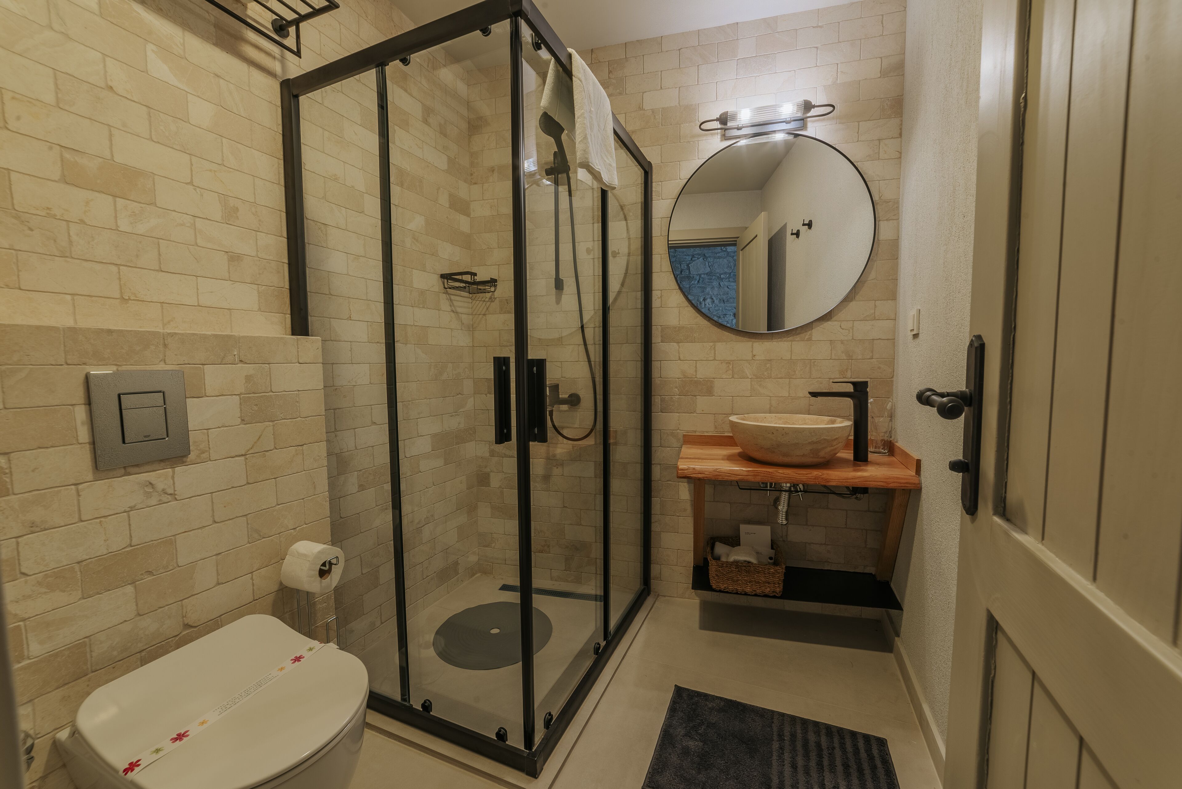 A bathroom with a glass-enclosed shower, a toilet, a sink with a wooden countertop, and a mirror on the wall.