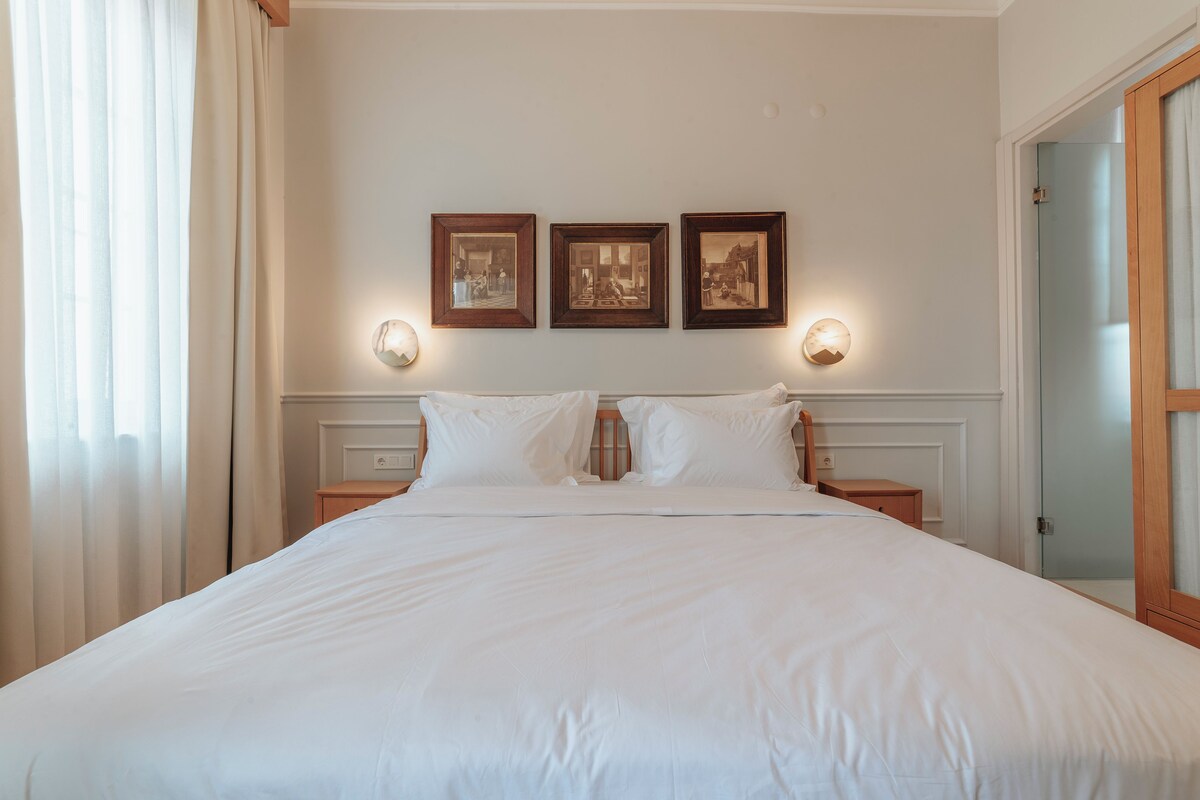 A neatly made bed with white linens, a wooden nightstand with a lamp, and three framed pictures on the wall.