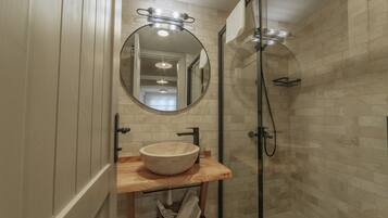 Un baño con tocador de madera, espejo redondo, lavamanos color beige y cabina de ducha con mampara de vidrio.