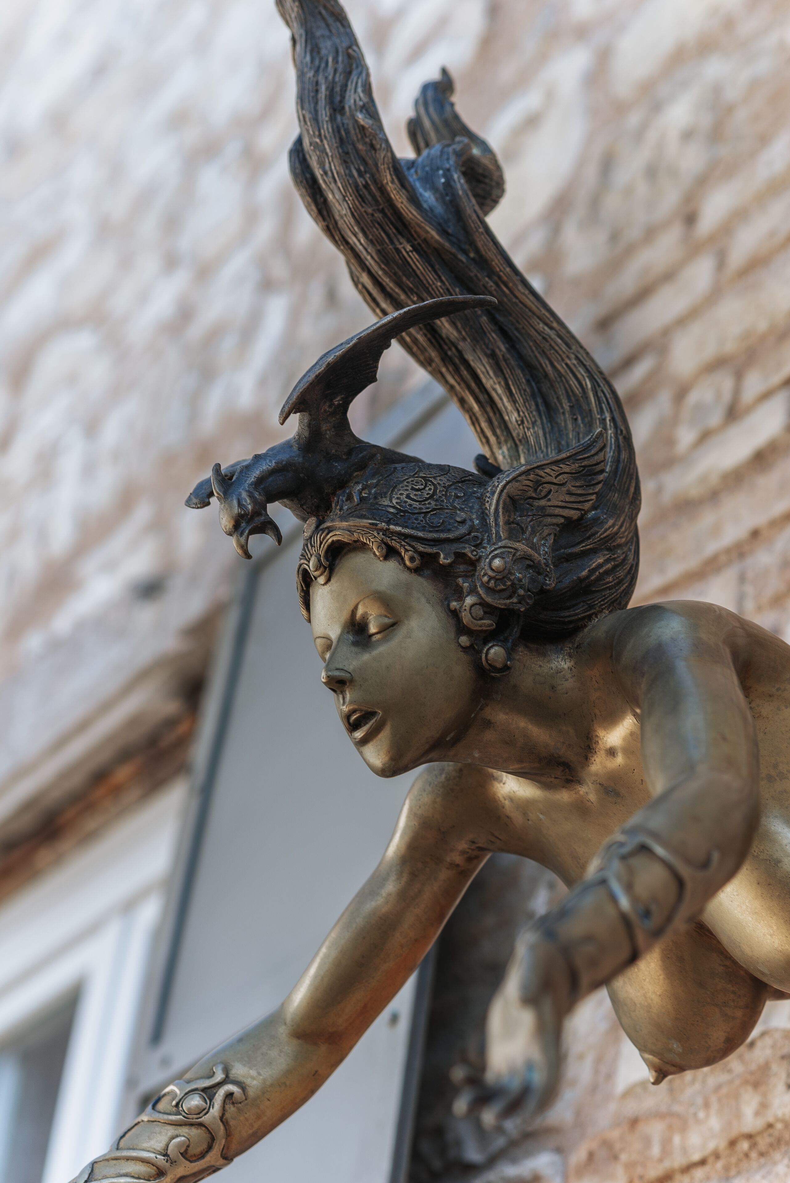A bronze statue of a winged figure with intricate details and a textured background.