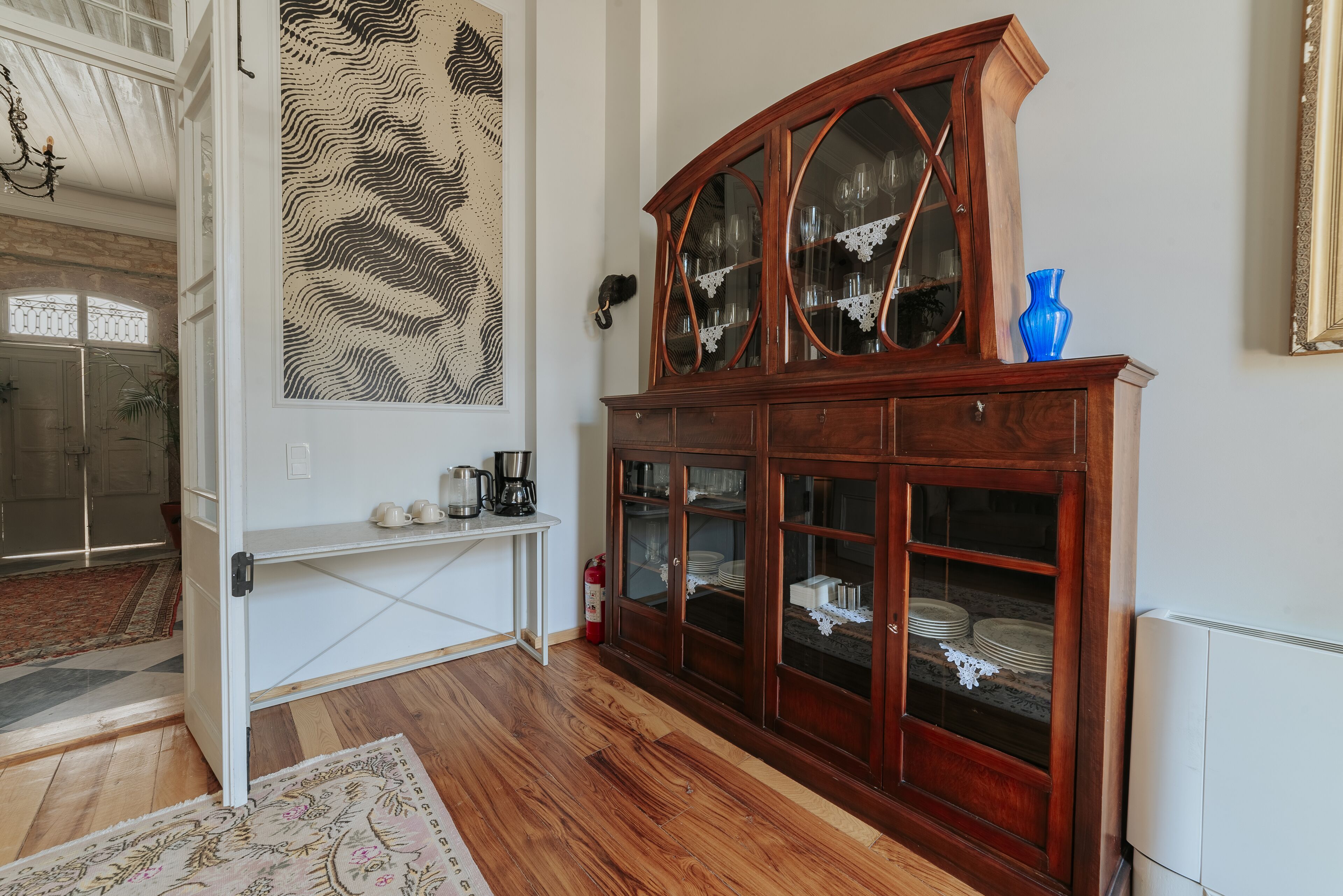 Een kamer met een houten kast voorzien van glazen deuren, een witte console tafel en een wanddecoratie met een patroon.