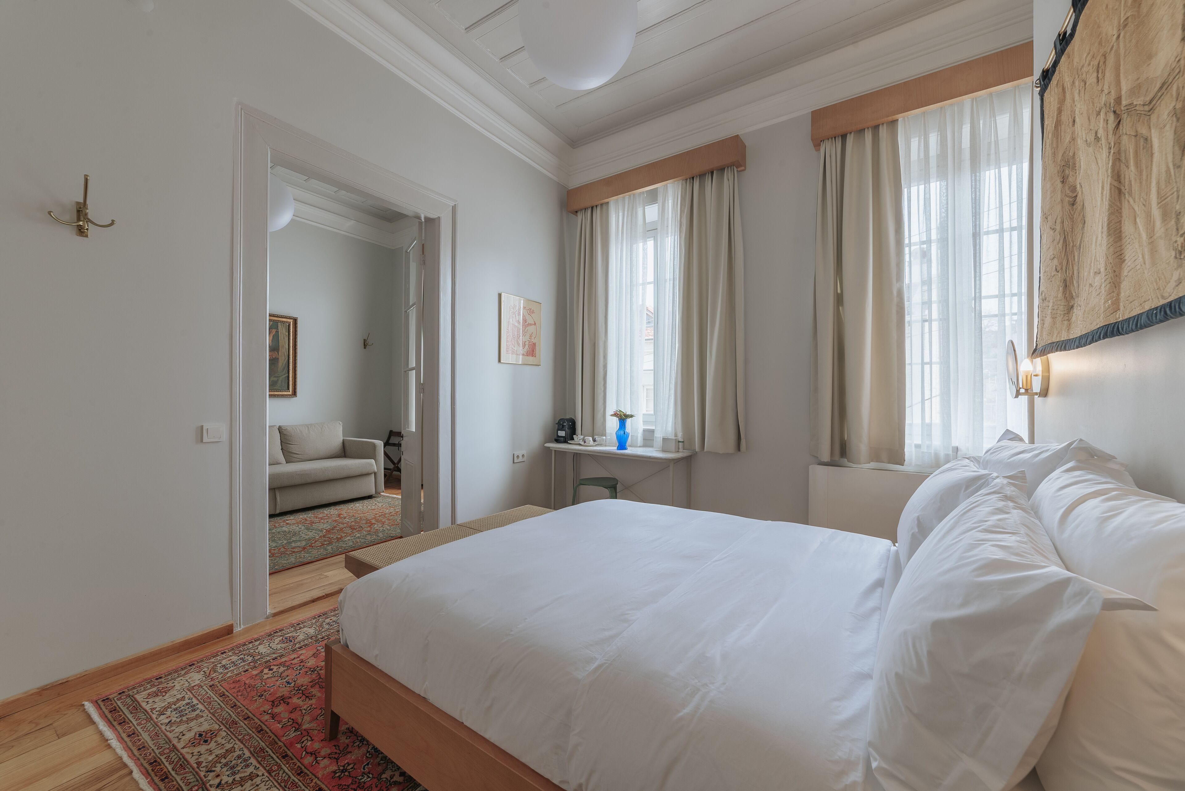 A bedroom with a large bed, a desk, a chair, and a window with curtains.