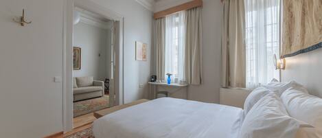 A bedroom with a large bed, a desk, a chair, and a window with curtains.