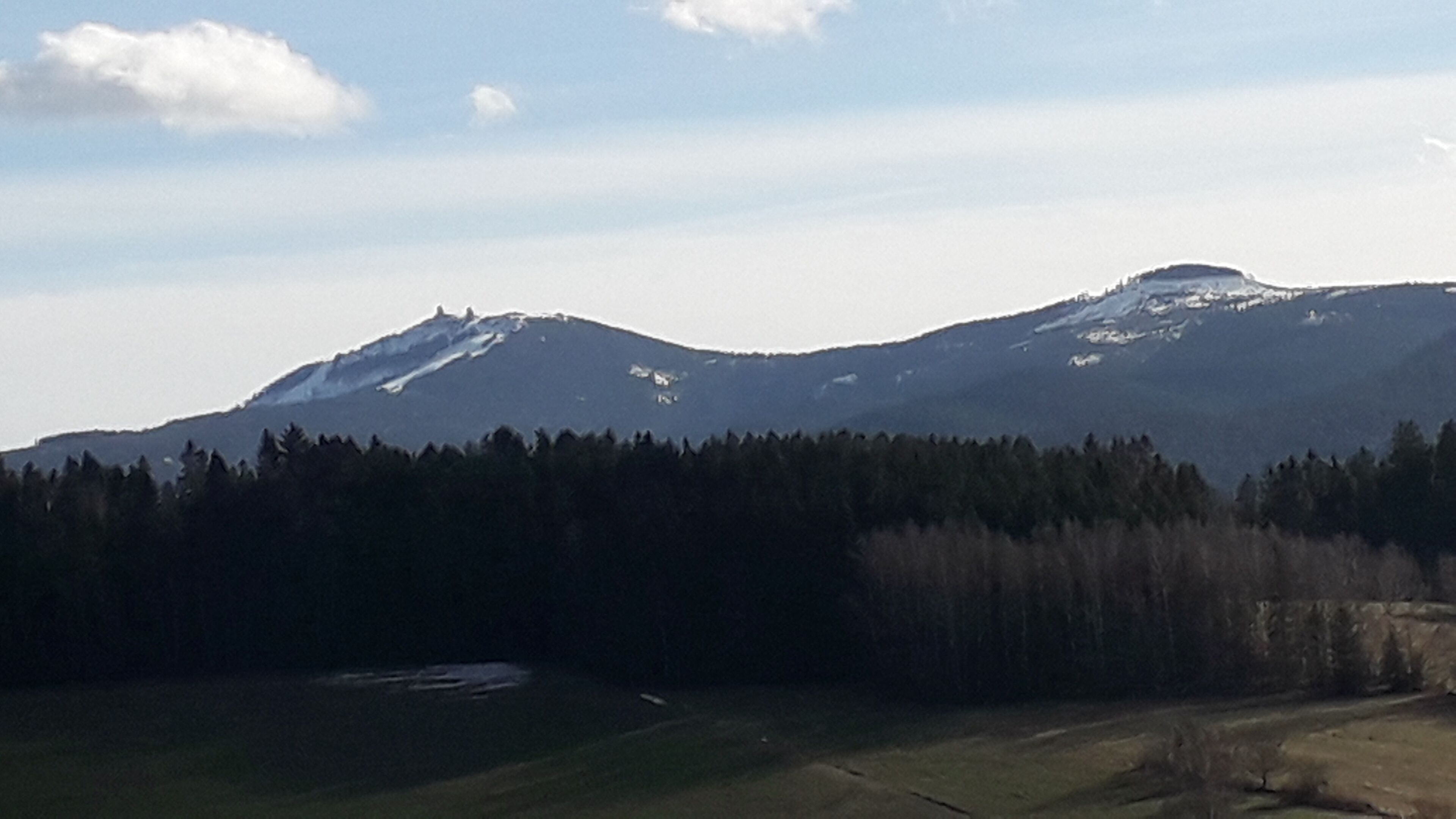 Un paysage montagneux avec une zone boisée au premier plan et un ciel dégagé au-dessus.