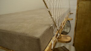 Una silla hamaca con cojín color beige, estructura de madera y un lateral de mosquitera.