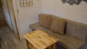 Una habitación con una mesa de madera, un sofá gris con dos cojines tejidos y una escalera de bambú apoyada en la pared.