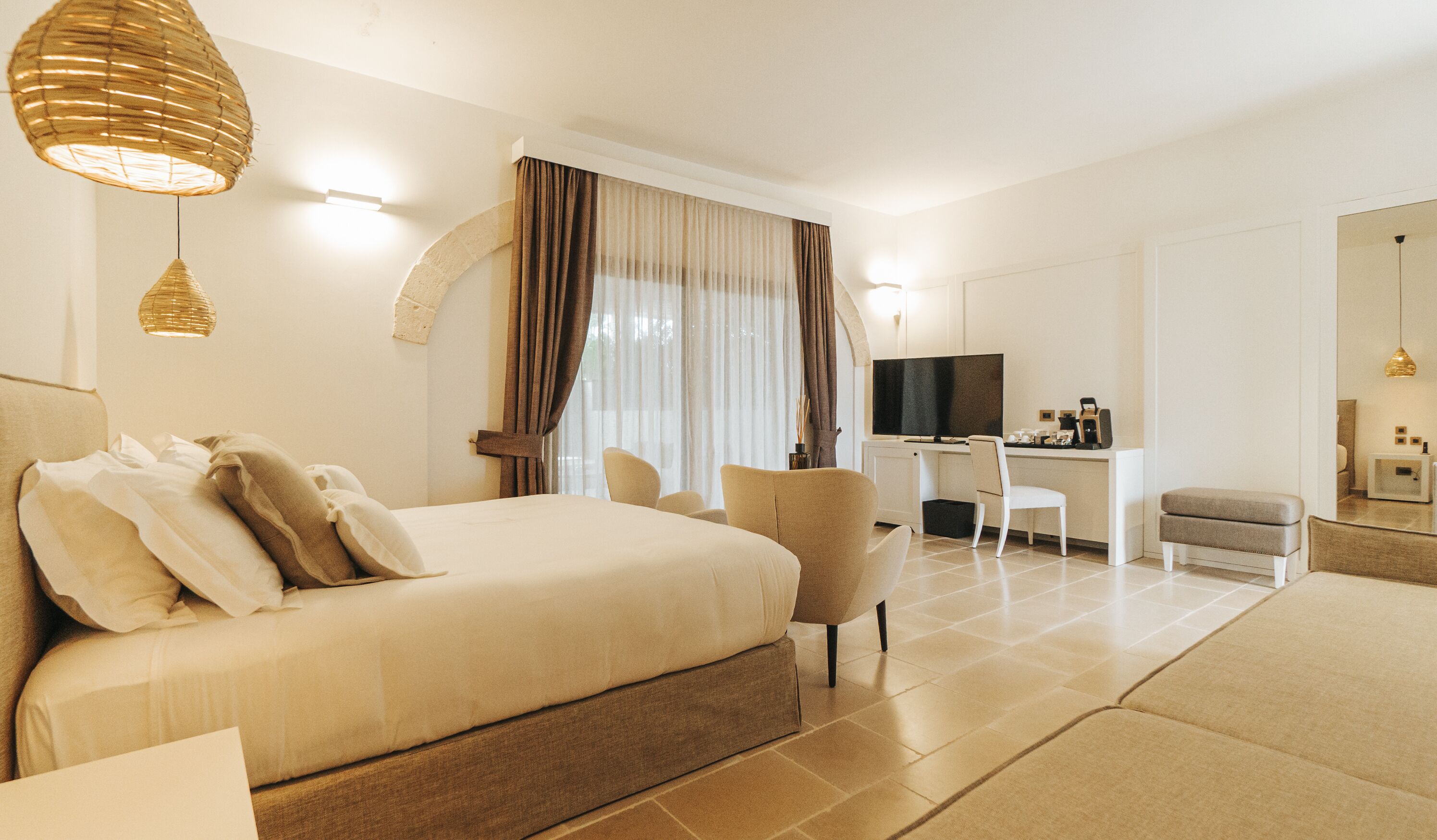 Quarto de hotel com cama, escrivaninha, cadeira, televisão e uma pequena mesa com cafeteira.
