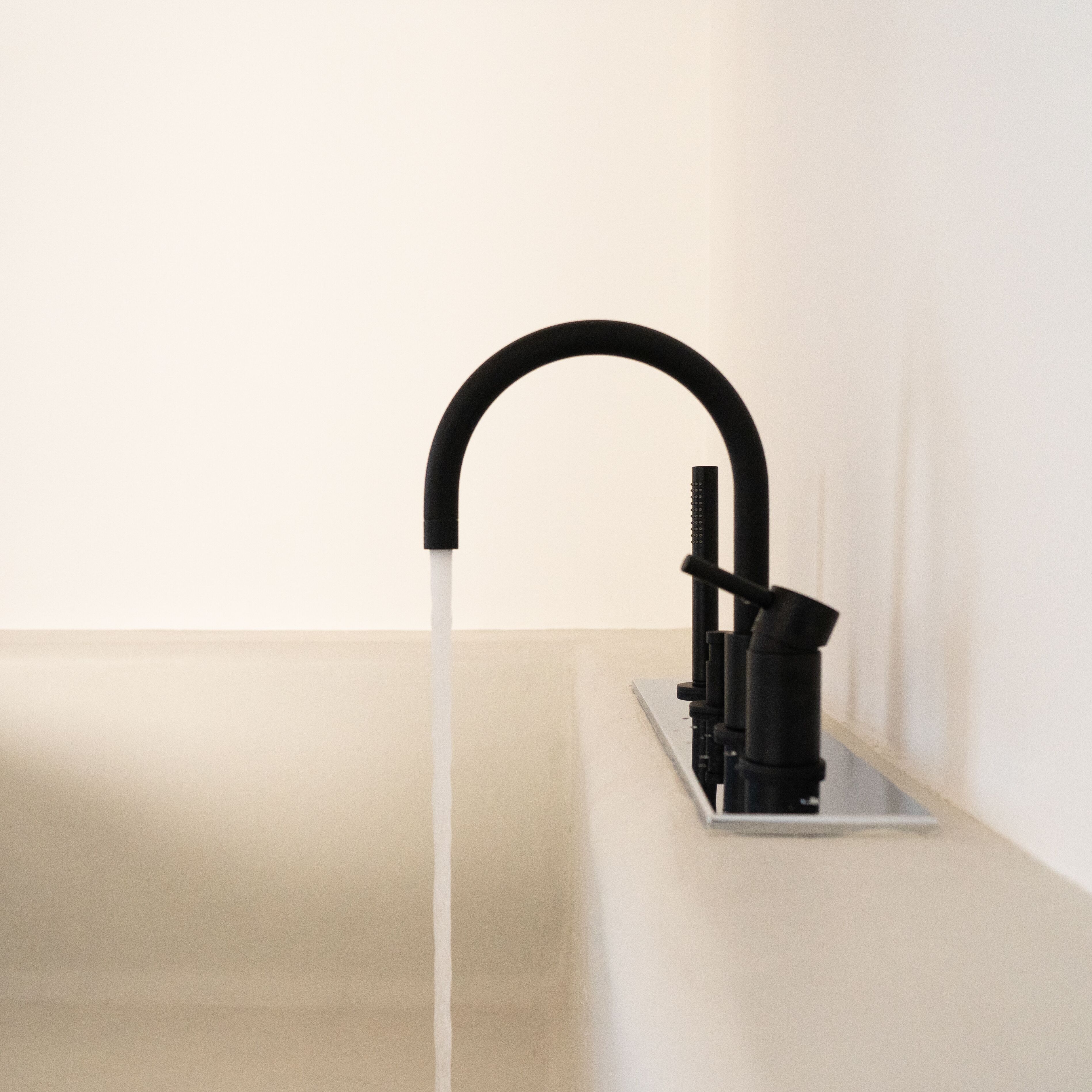 A modern faucet with a curved spout and a water stream flowing from it, mounted on a metallic surface against a plain wall.