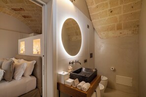 A modern bathroom with a large oval mirror, a wooden vanity, a black sink, and a white toilet.