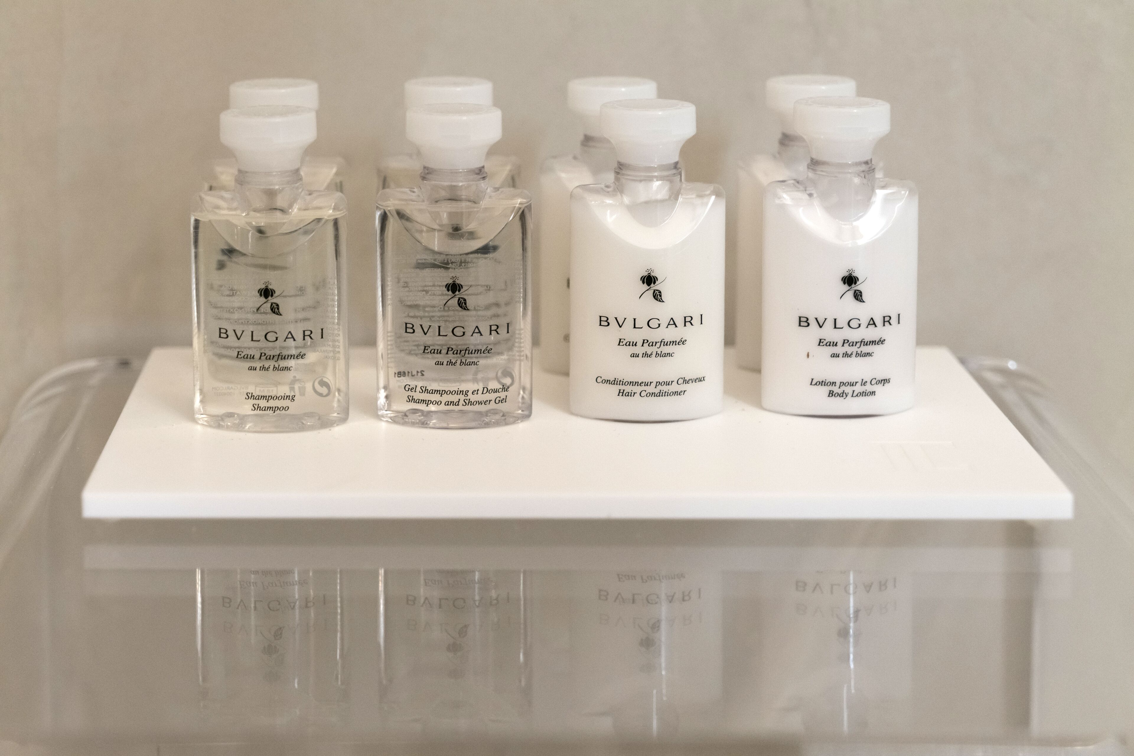 Four bottles of Bylgari body lotion on a white shelf.