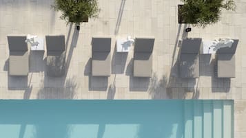 Vue aérienne d’un espace autour d’une piscine, avec des chaises longues et deux arbres.