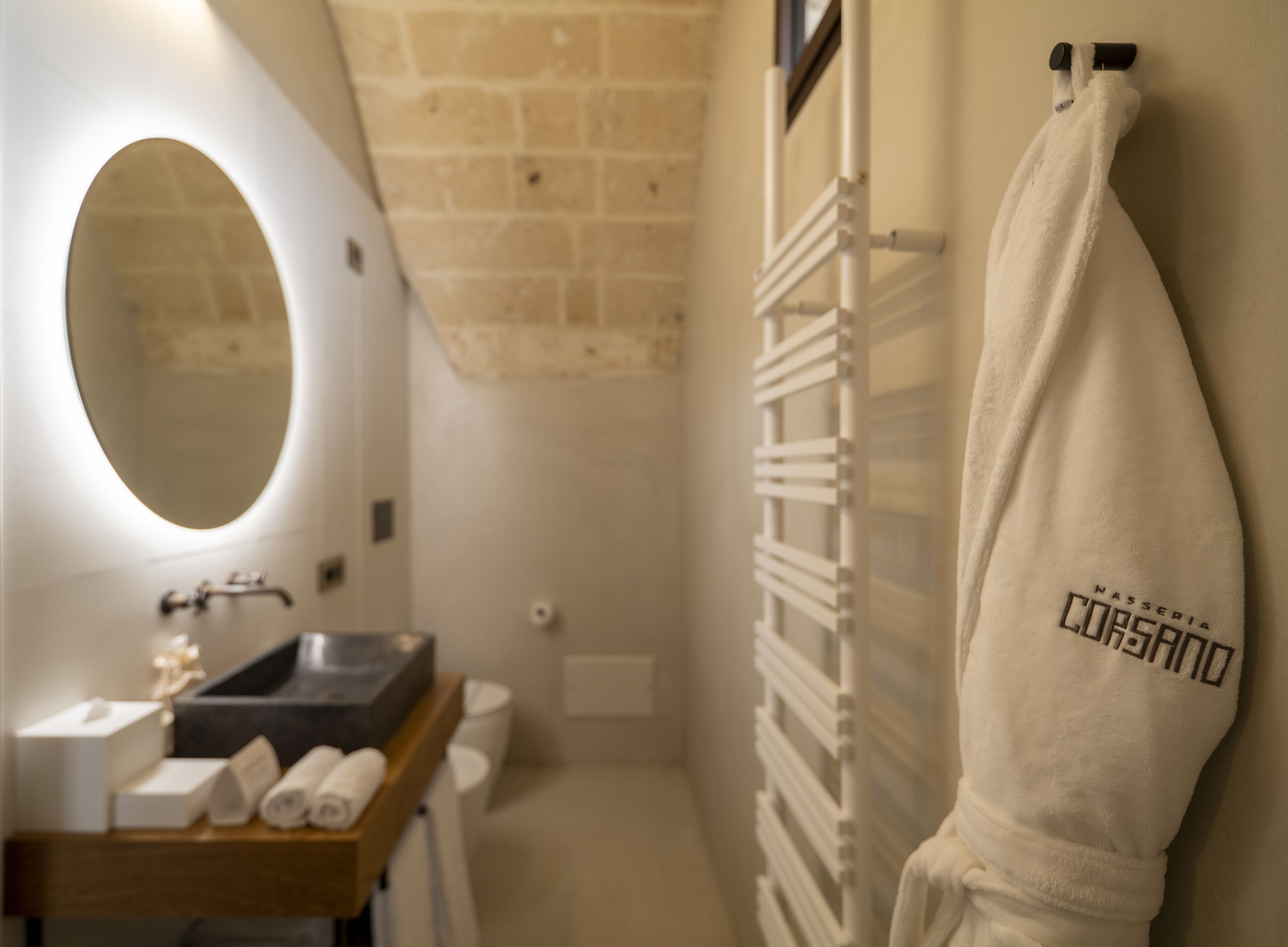 A bathroom with a wooden vanity, a round mirror, a towel rack with a towel, and a radiator.