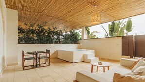 A modern, open-plan living area with a high ceiling, a seating area with a sofa and a coffee table, a dining table with chairs, and a large window overlooking a lush garden. - Masseria Corsano (Nardò)