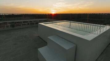 Une piscine extérieure moderne, dotée d’une paroi en verre et de marches, qui se détache sur le décor d’un coucher de soleil.