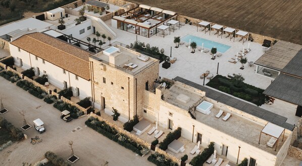 An aerial view of a hotel with multiple pools, outdoor seating areas, and a large building with a stone facade.