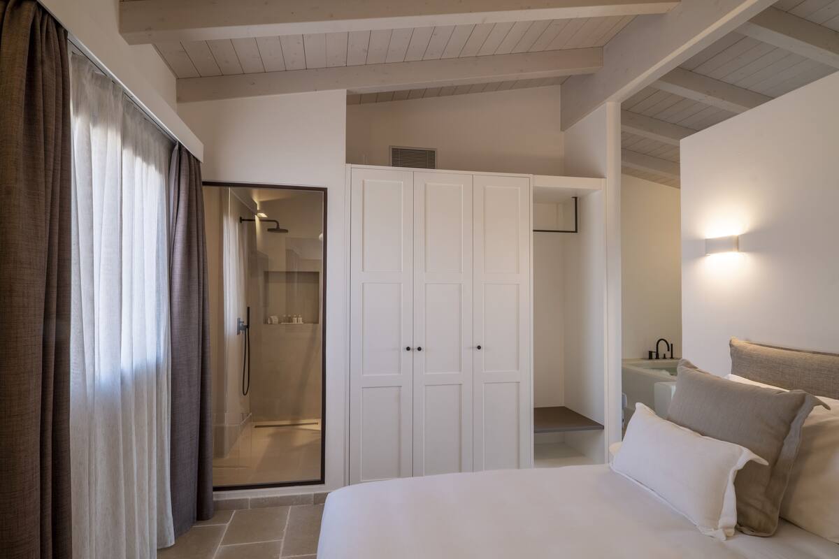 Une chambre dotée d’un grand lit, d’un dressing, d’un espace douche et d’une salle de bain avec un lavabo et un miroir.
