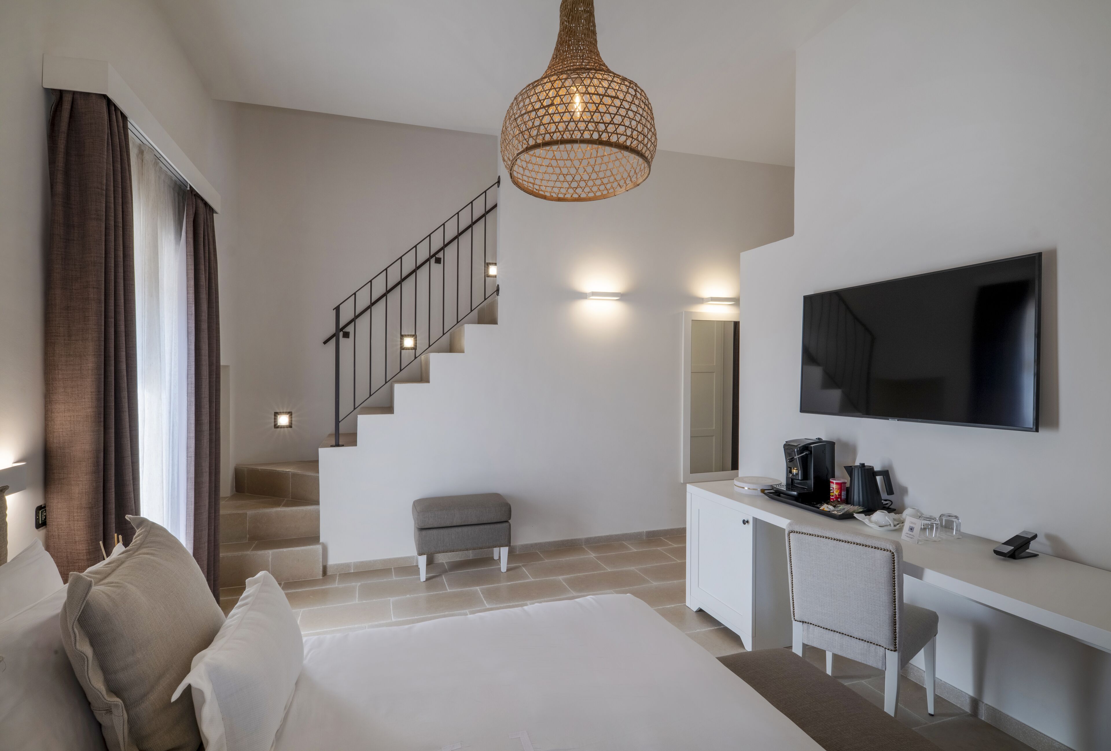 Habitación de hotel moderna con escalera, televisor de pantalla plana, escritorio con cafetera y una cama grande.