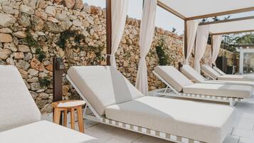 A sunlit outdoor lounge area with stone walls and cushioned lounge chairs.