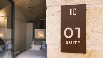 Letrero de hotel que indica la habitación número 01, suite, con una cama visible y una puerta de vidrio que da a otra habitación.