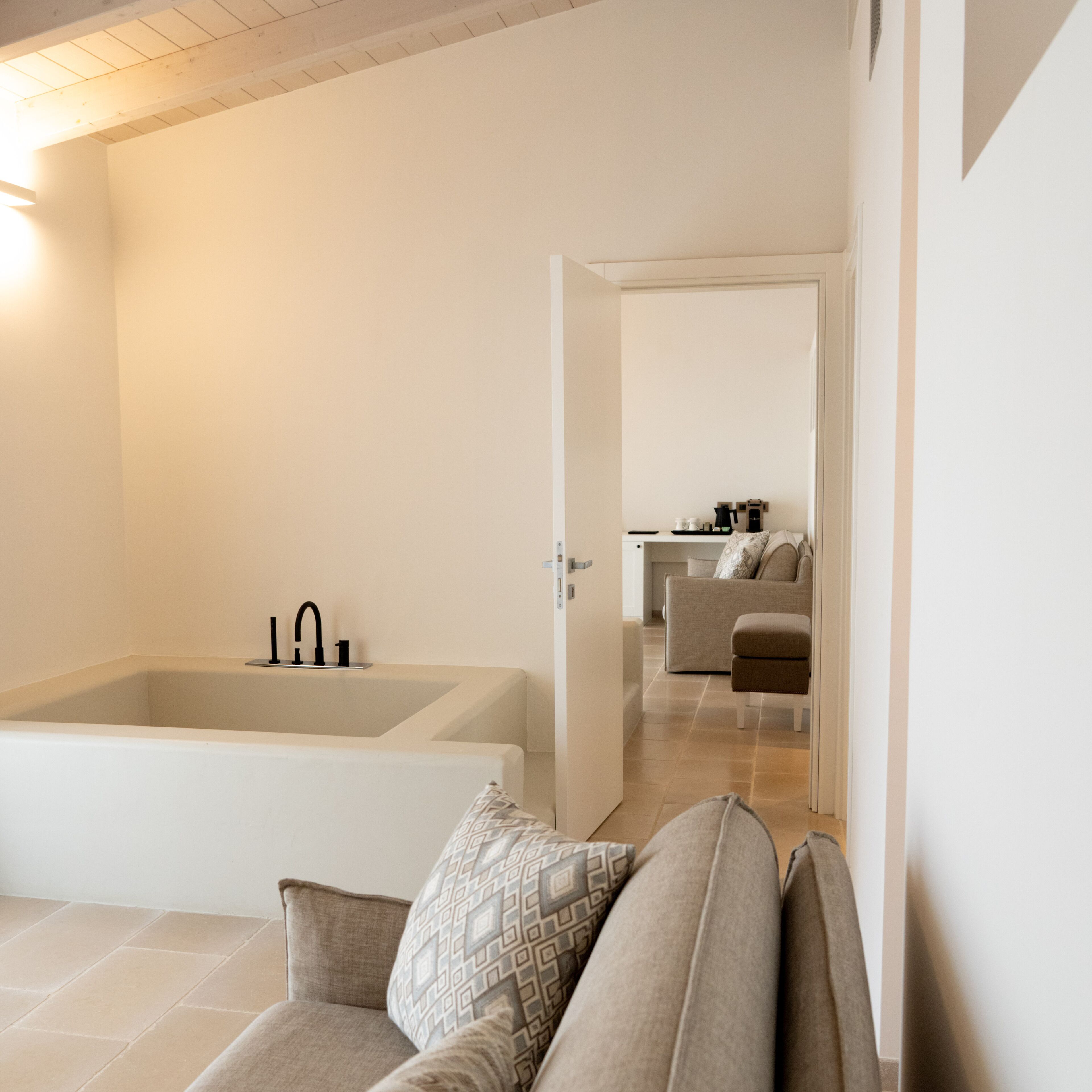 A modern bathroom with a bathtub and a shower. There is a sofa with patterned cushions in the foreground.