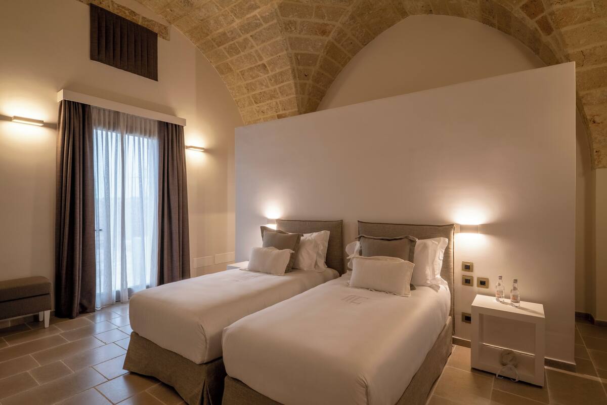 Une chambre d’hôtel avec deux lits, un banc, une table de chevet et un grand plafond en arc de cercle.