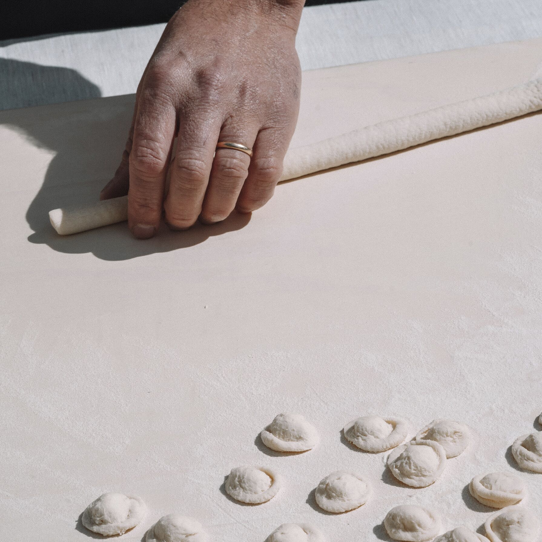 A hand rolling dough on a flat surface with several dough balls scattered around.