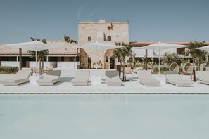 A poolside area with lounge chairs and umbrellas, a brick building in the background, and a clear sky.