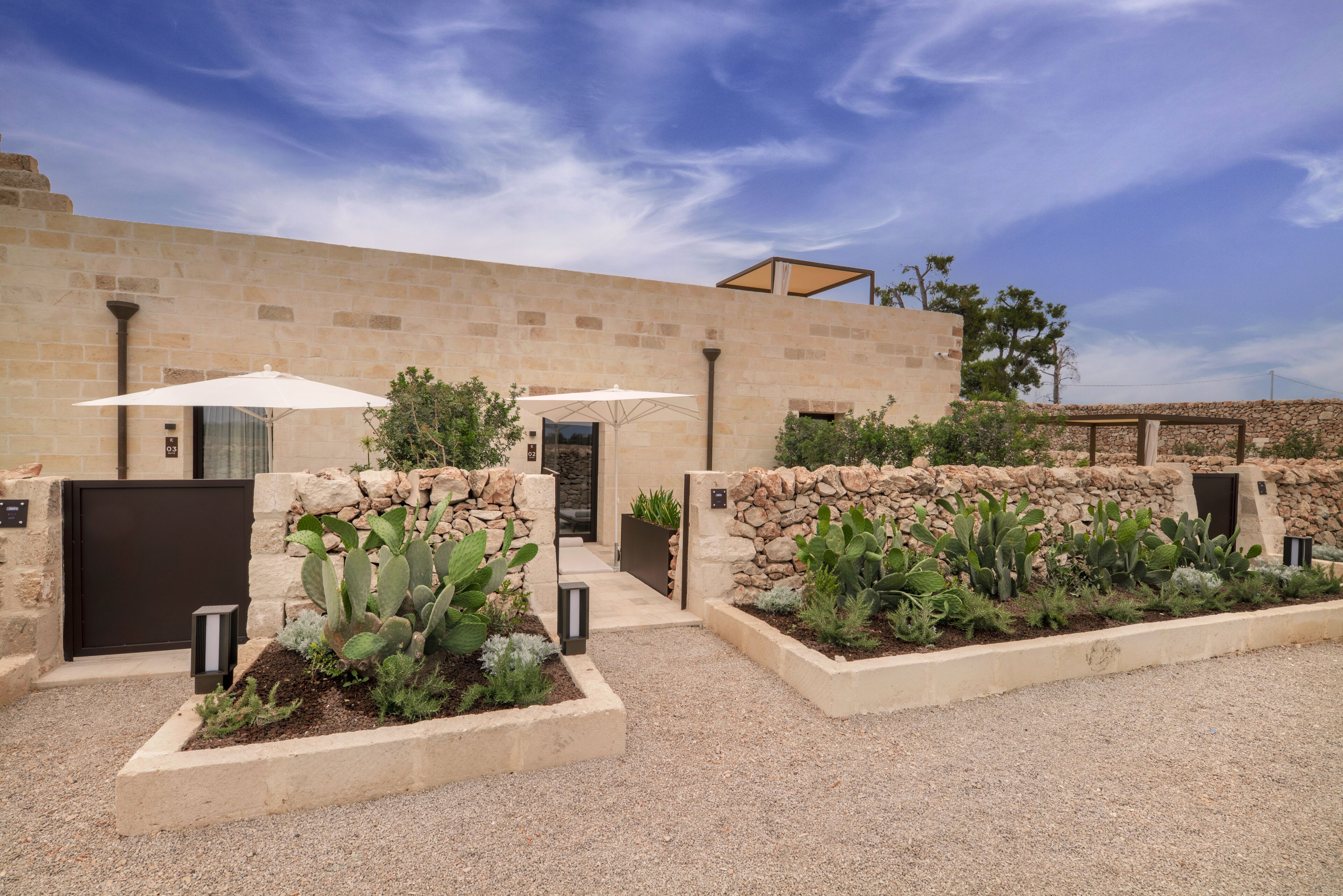 A courtyard with a stone wall, cactus plants, and two umbrellas.