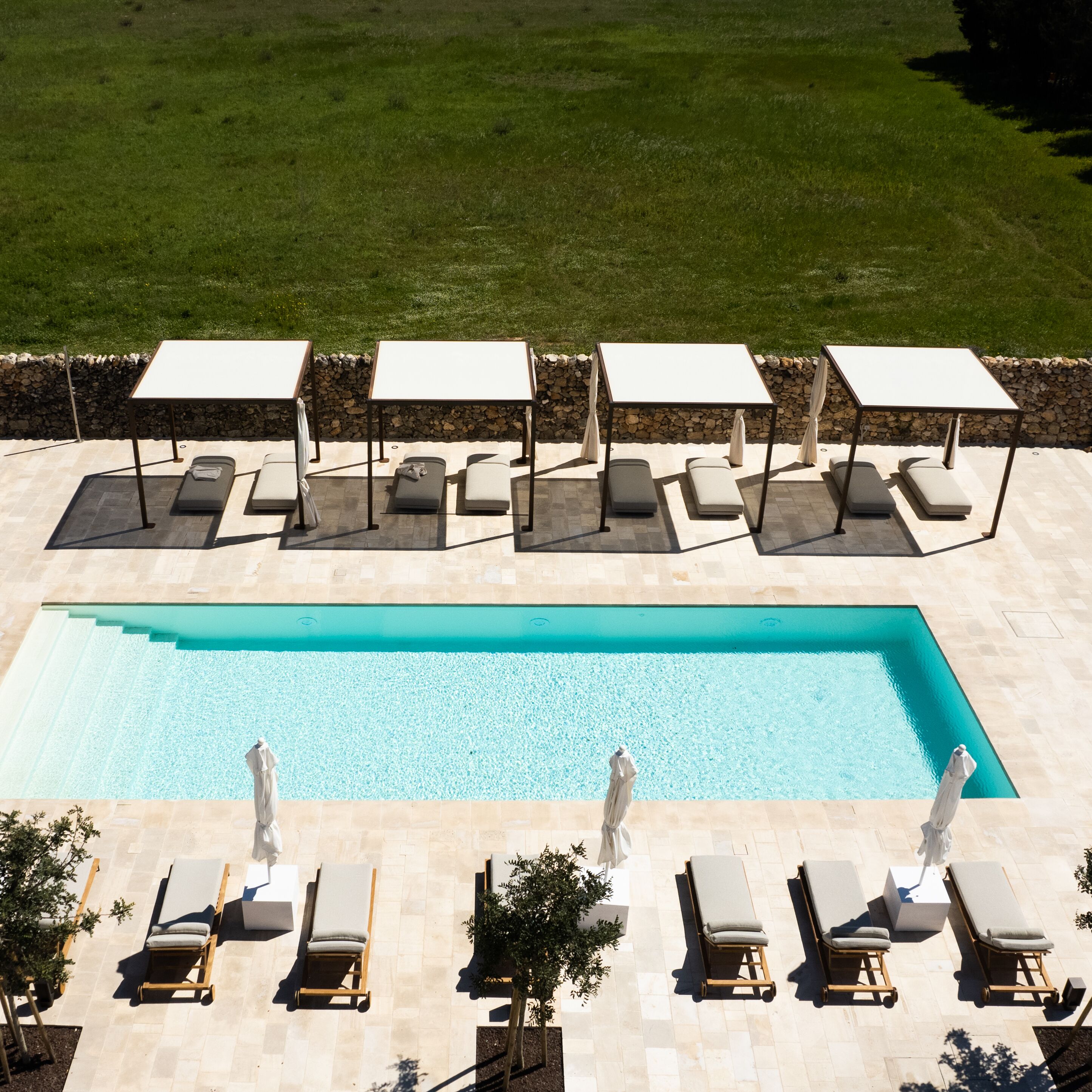 A rectangular swimming pool with lounge chairs and umbrellas arranged around it.