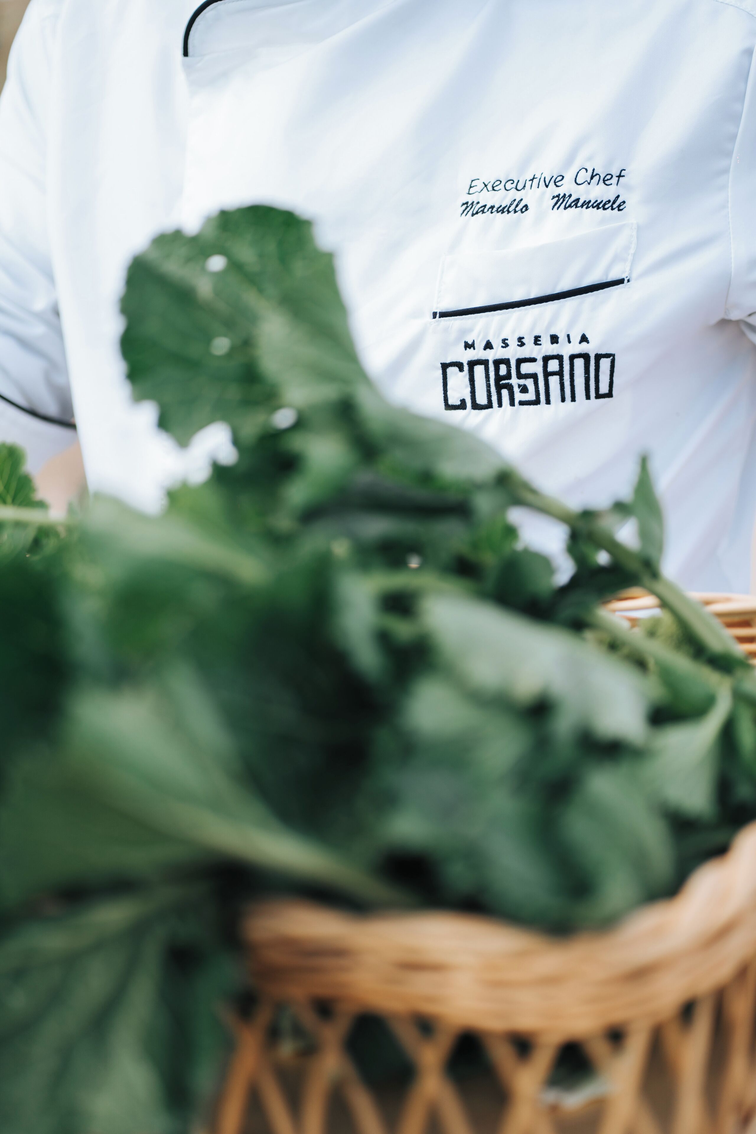 A person wearing a white chef's uniform with text indicating an executive chef position and a name.