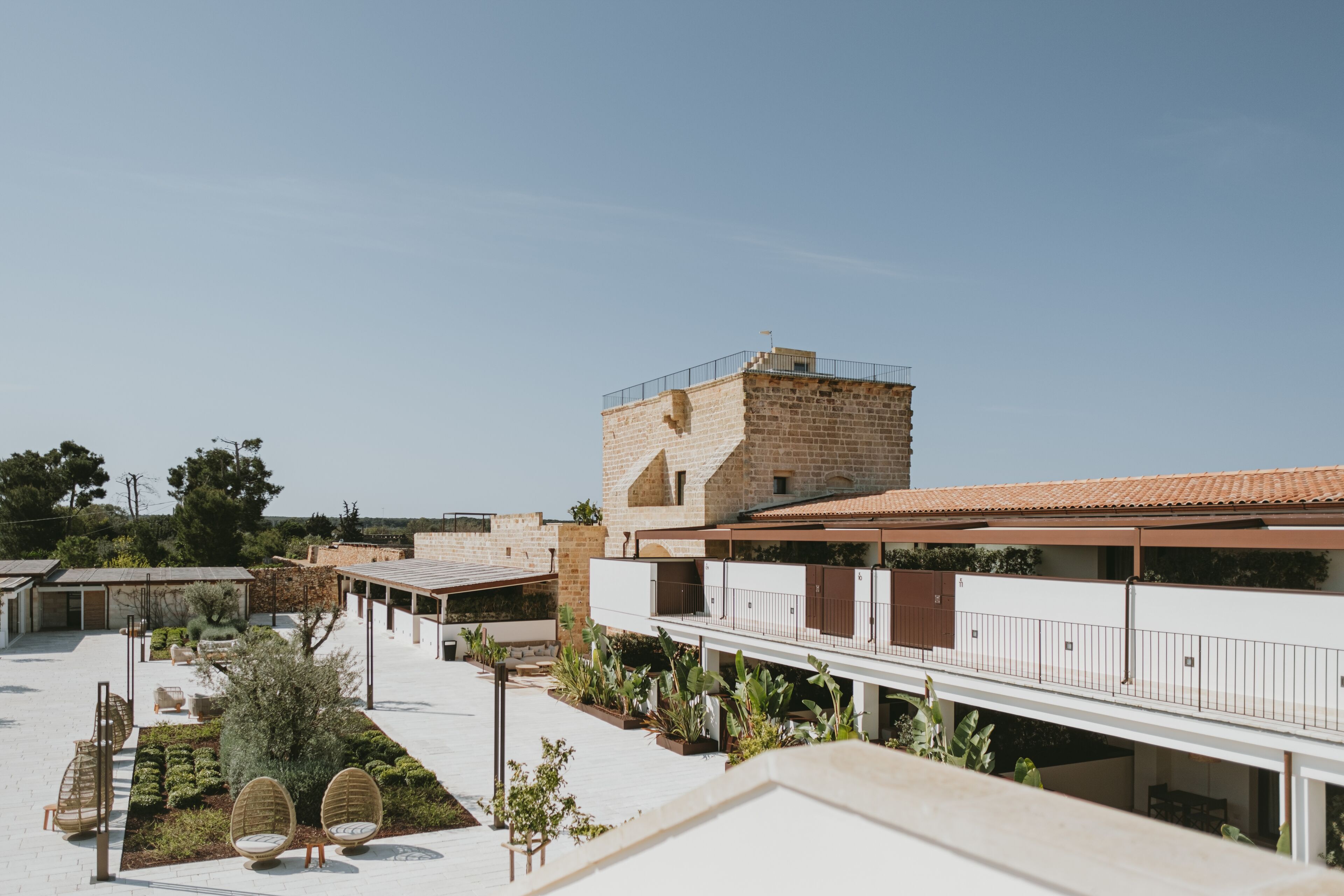 Un patio con un edificio de piedra, asientos al aire libre y cielo despejado.