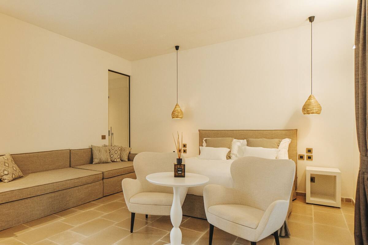 Une chambre d’hôtel moderne, équipée d’un canapé, de deux fauteuils, d’une petite table ronde et d’un lit avec une tête de lit.