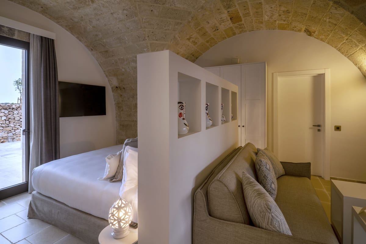 Une chambre avec un lit, un canapé, une télévision et un mur en pierre.