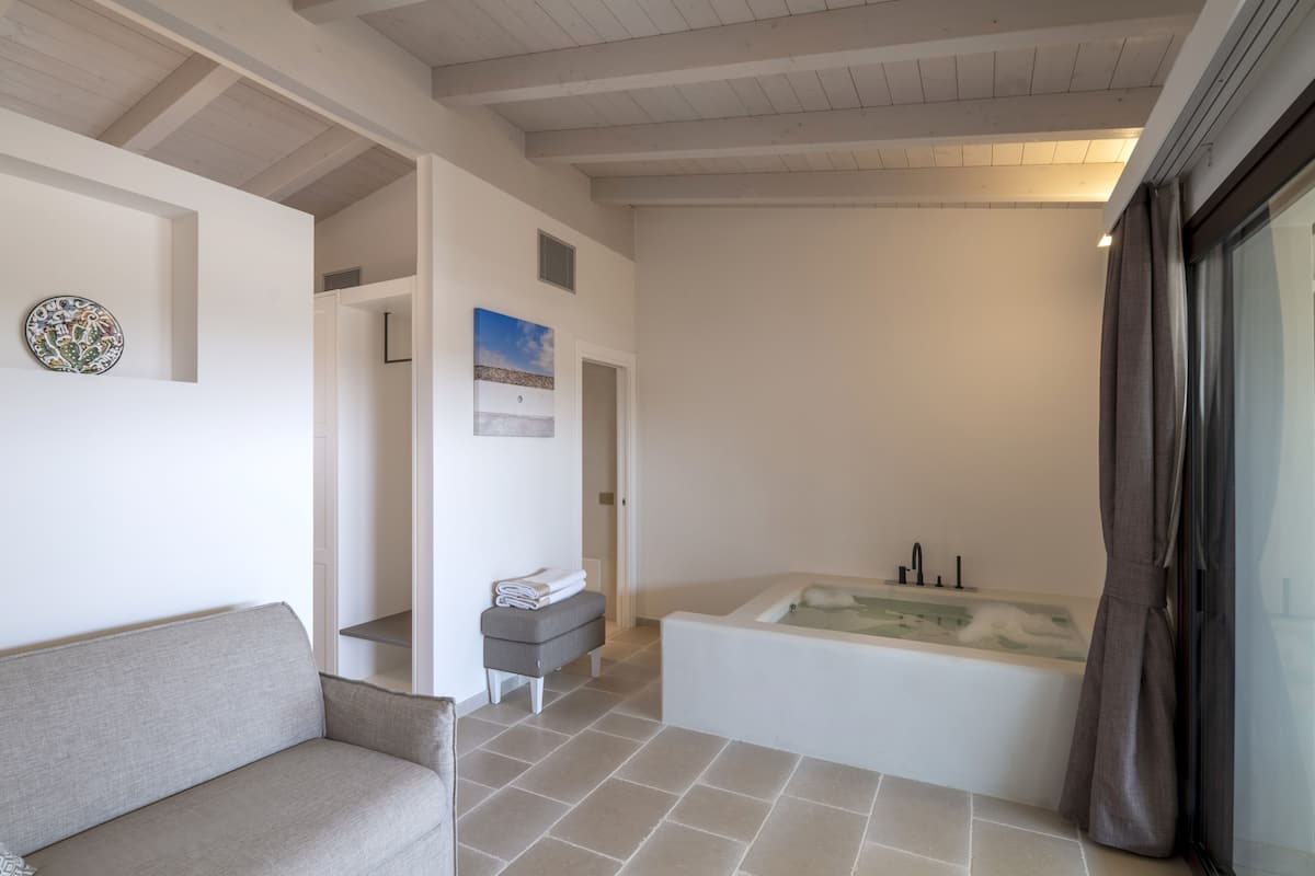 Une salle de bain moderne avec une baignoire, des toilettes et un lavabo. On y trouve un porte-serviettes et un petit banc. Le sol est carrelé et les murs sont blancs.