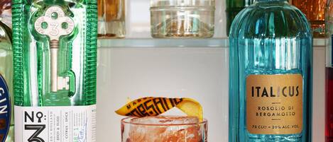 A variety of liquor bottles, including No. 3 London Dry Gin and Italian Cus Rosolio di Bergamotto, alongside a glass of cocktail.