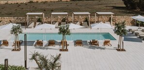 A poolside area with lounge chairs and umbrellas, a stone wall in the background, and a clear blue pool.