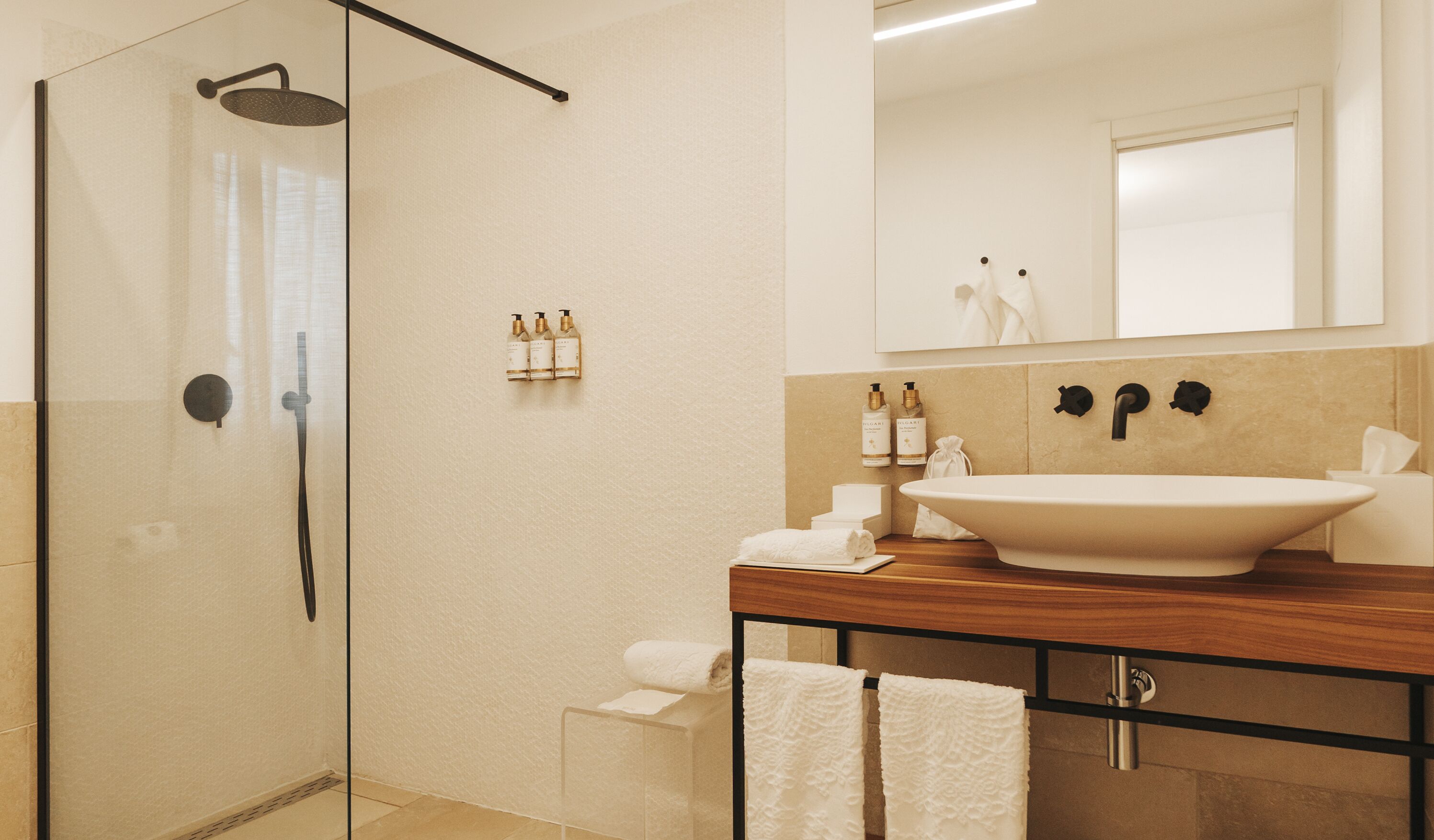 A modern bathroom with a glass shower enclosure, a large sink, and toiletries on the vanity.