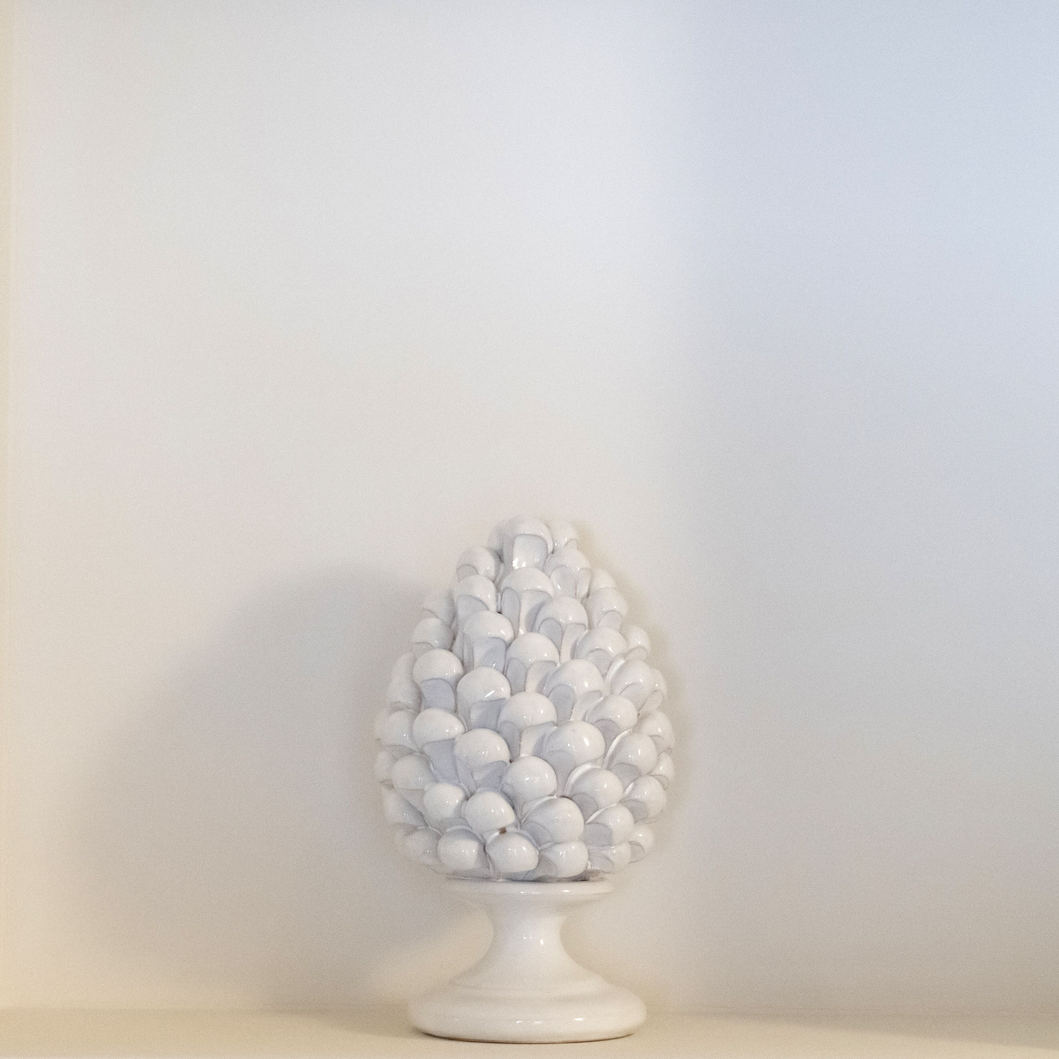 A white ceramic vase with a spherical design on a white pedestal against a plain wall.