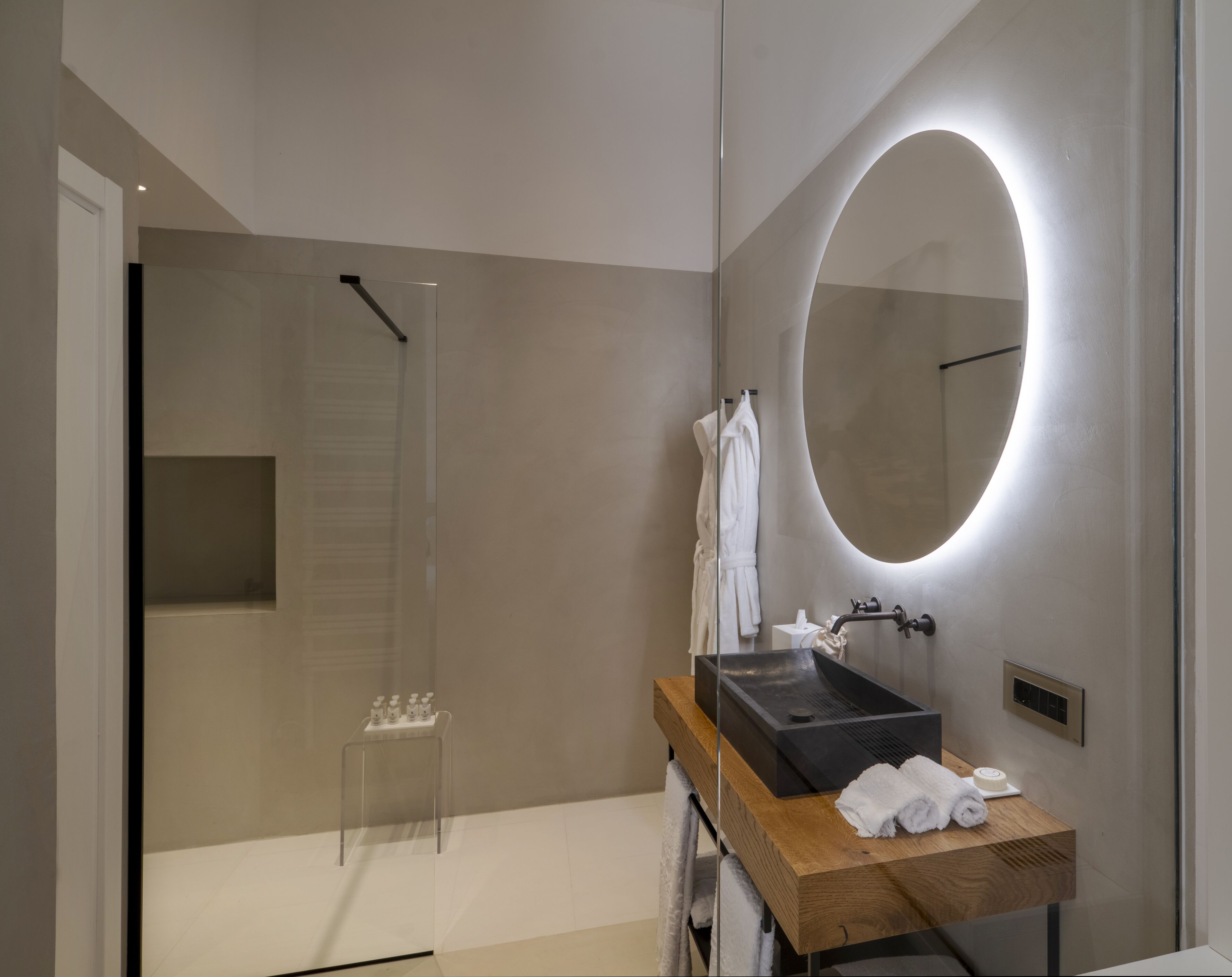 A modern bathroom with a wooden vanity, a large mirror, a glass shower enclosure, and a towel rack.