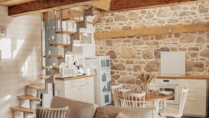 Un salon confortable avec un canapé, une table à manger avec des chaises, un coin cuisine avec une cuisinière et un escalier doté d’une rampe en métal.